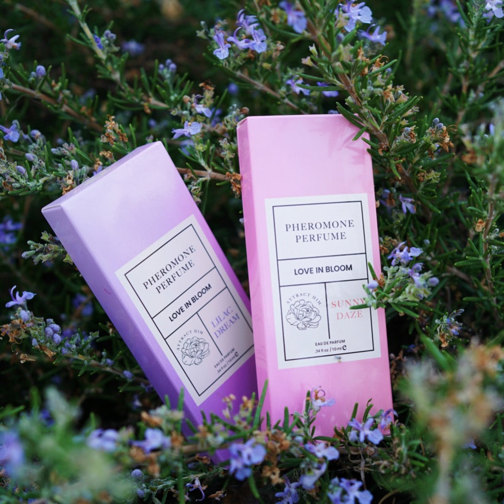 LOVE IN BLOOM Pheromone Perfumes - Lilac Dream and Sunny Daze displayed against a backdrop of wildflowers.