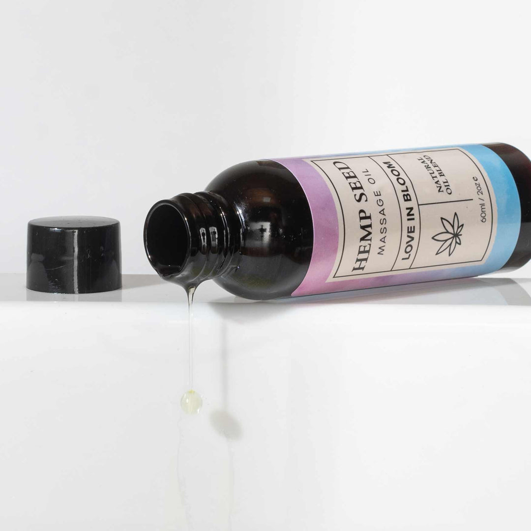 Open bottle of Eye of Love's Hemp Seed Massage Oil lying on its side with a stream of oil dripping out